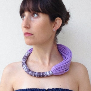 Peut inclure: Une femme portant une robe bleue sans bretelles avec un collier en tissu violet. Le collier est compos&eacute; de plusieurs couches de tissu et est nou&eacute; &agrave; l'arri&egrave;re du cou.