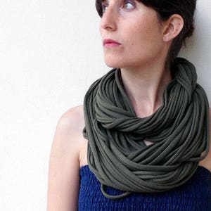 May include: A woman wearing a dark green infinity scarf and a dark blue dress. The scarf is made of a soft, stretchy fabric and is worn around the neck.
