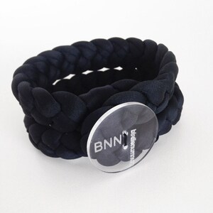 May include: Black braided fabric bracelet with a clear button that says "BNN birdeye.com".
