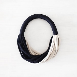 May include: A black and beige fabric necklace with a simple, modern design.