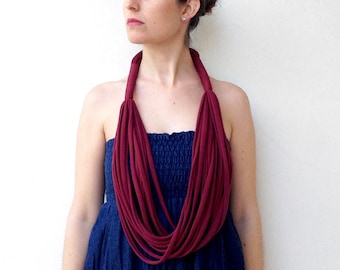 Puede incluir: Una mujer con un vestido azul oscuro y un collar de tela color burdeos. El collar está hecho de múltiples hebras de tela, creando un efecto de capas.