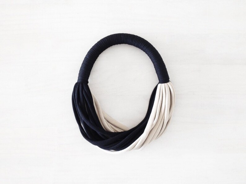 May include: A black and beige fabric necklace with a simple, modern design.