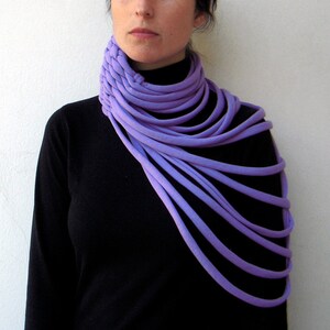 May include: A purple fabric neck scarf with multiple layers, worn by a person with a black turtleneck shirt.