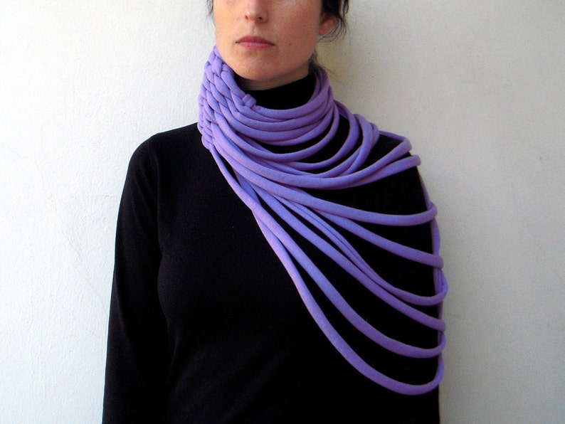 May include: A purple fabric neck scarf with multiple layers, worn by a person with a black turtleneck shirt.