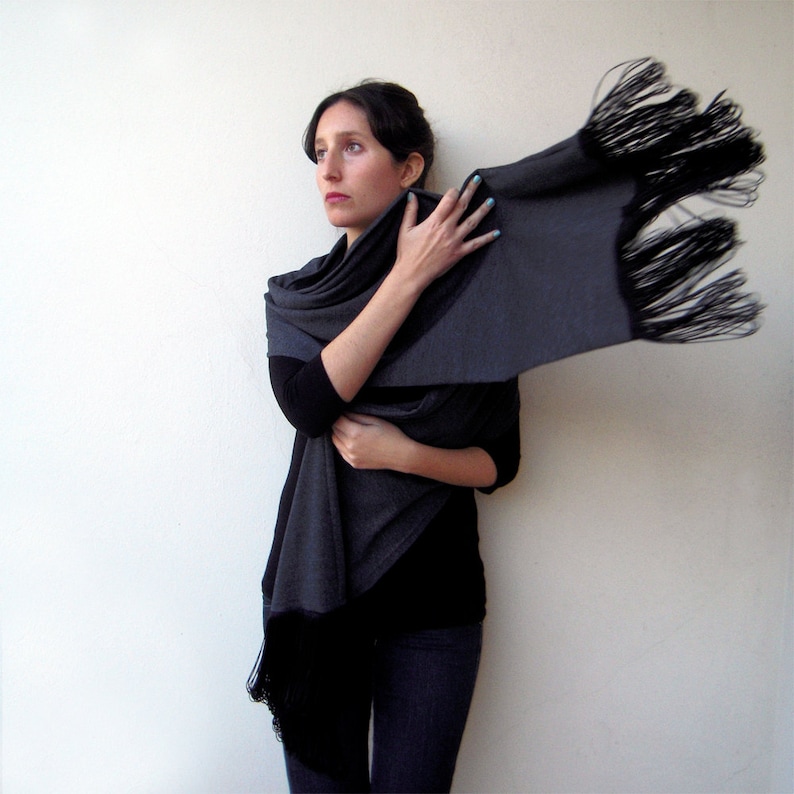 May include: A gray shawl with black fringe, worn by a person with dark hair and blue nail polish.