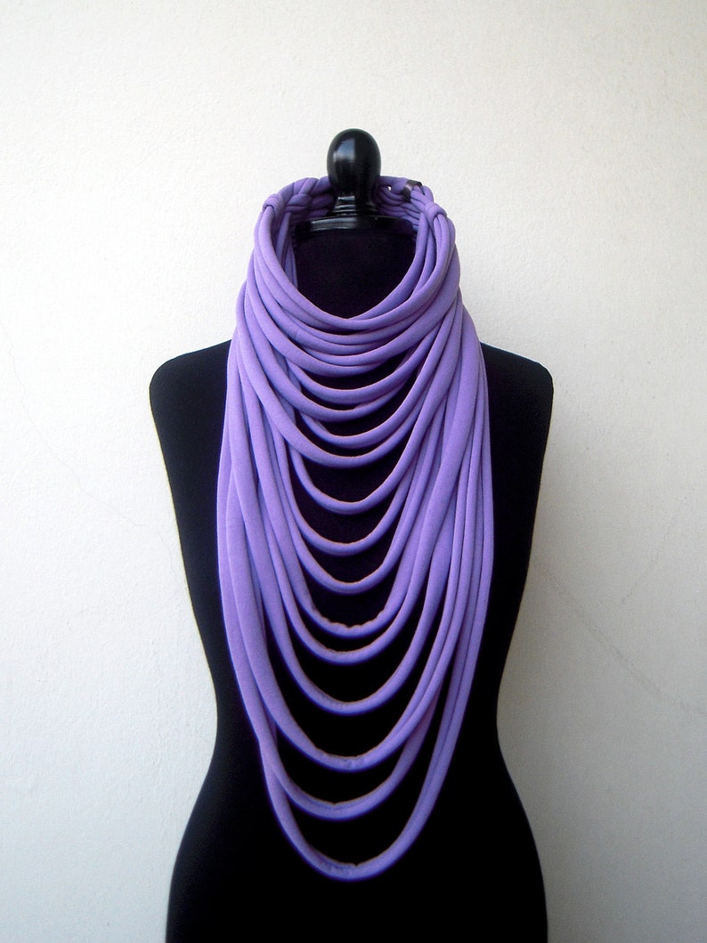 May include: A long, layered purple scarf made of fabric. The scarf is draped around a black mannequin.