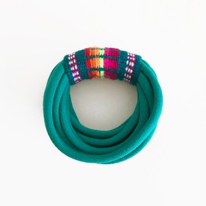 May include: Teal fabric headband with a colourful woven stripe detail.