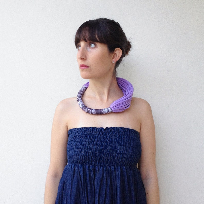 Peut inclure: Une femme portant une robe bleue sans bretelles avec un collier en tissu violet. Le collier est compos&eacute; de plusieurs couches de tissu et est nou&eacute; &agrave; l'arri&egrave;re du cou.