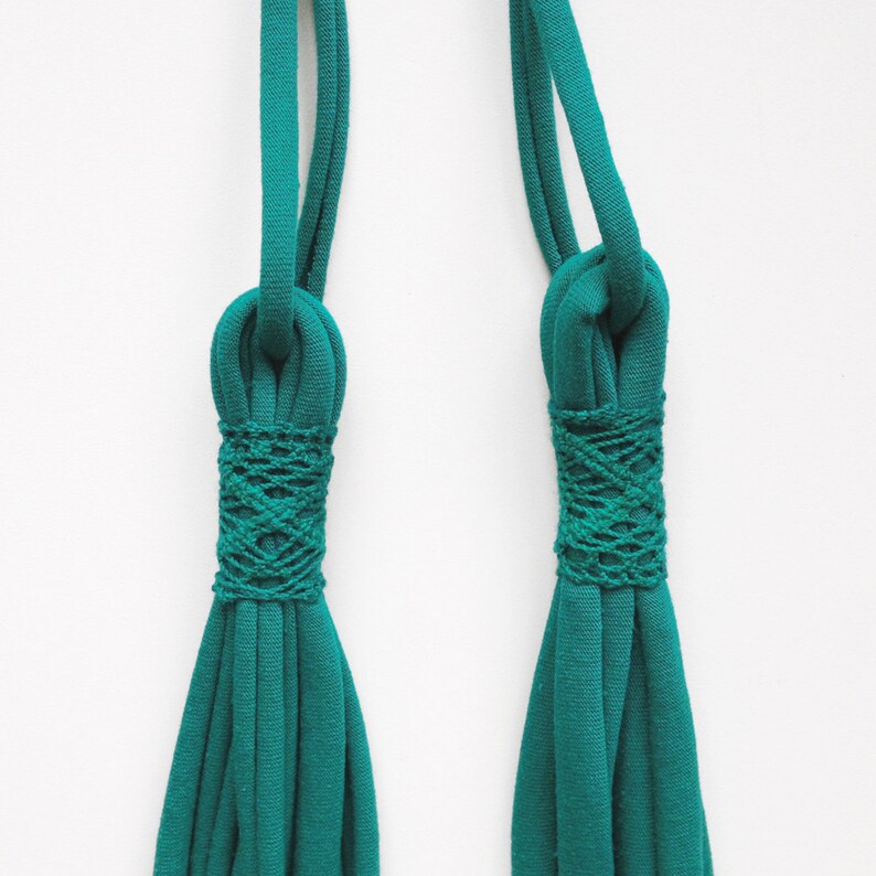 May include: Two teal green fabric cords with a knotted design at the top. The cords are tied together with a woven pattern.