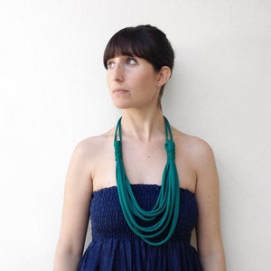 May include: A woman wearing a teal blue layered necklace with a navy blue strapless dress.