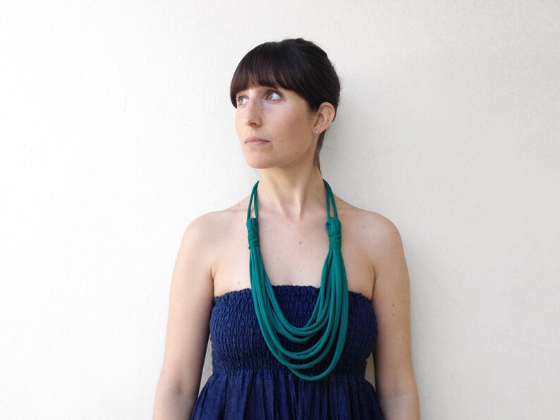 May include: A woman wearing a teal blue layered necklace with a navy blue strapless dress.