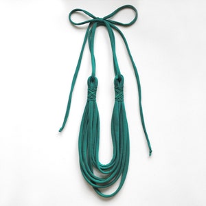 May include: Teal blue fabric necklace with a knotted design. The necklace is made of multiple strands of fabric and has a long, thin tie at the top.