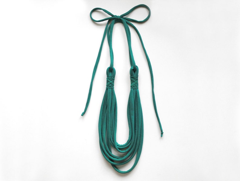 May include: Teal blue fabric necklace with a knotted design. The necklace is made of multiple strands of fabric and has a long, thin tie at the top.
