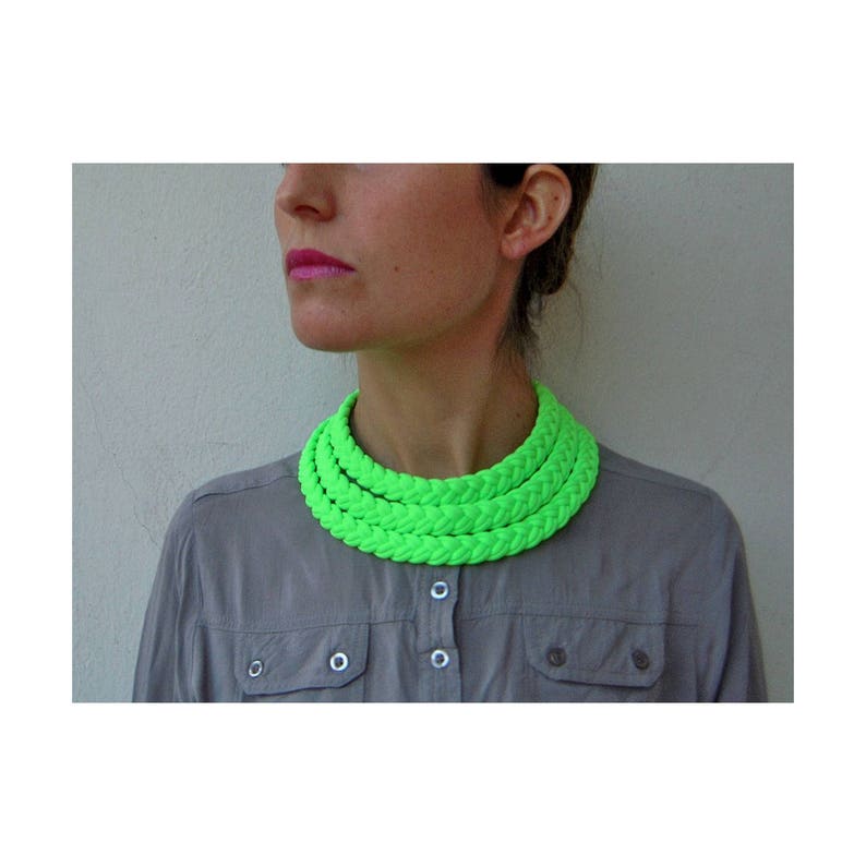 May include: A bright green multi-layered necklace made of braided rope. The necklace is worn by a person with a gray shirt.