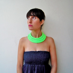 May include: A woman wearing a strapless black dress with a bright green layered necklace.