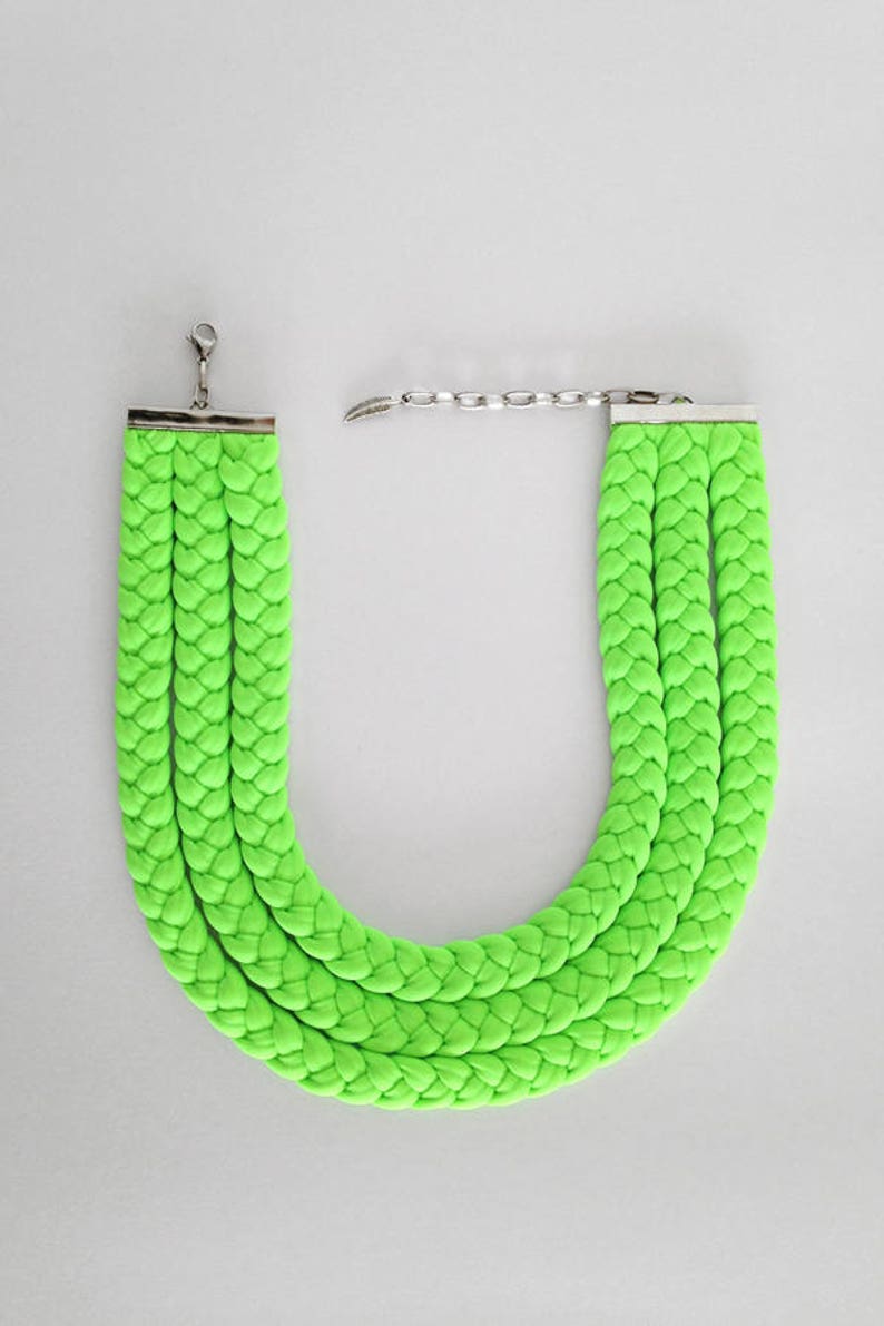 May include: A bright green braided necklace with a silver clasp. The necklace is made of three strands of braided fabric.