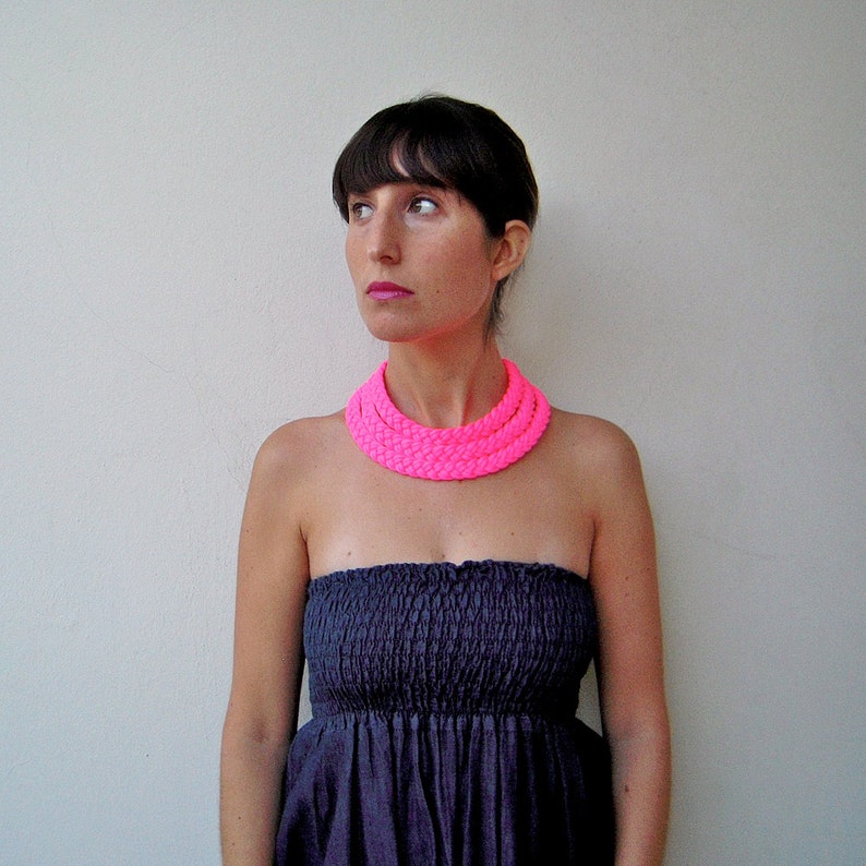 May include: A woman with short dark hair is wearing a strapless black dress and a bright pink multi-layered necklace.