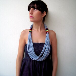 May include: A woman wearing a gray t-shirt fabric necklace with colorful accents. The necklace is layered and creates a thick, chunky look. The woman is wearing a black strapless dress.