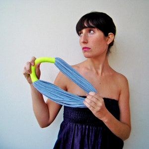 Peut inclure: Une femme porte un collier en tissu bleu et jaune fluo. Le collier est fait d'une longue bande de tissu qui est torsadée et nouée. La femme porte une robe bleue sans bretelles.