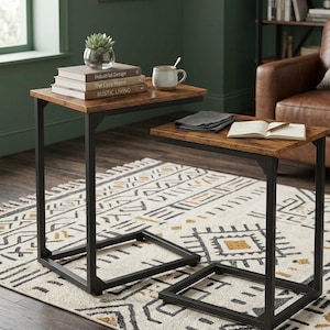 May include: Two brown and black side tables with a rustic wood-look top and a black metal frame. One table has books, a small plant, and a mug. The other table has a book and a folded cloth. The tables are on a patterned rug.