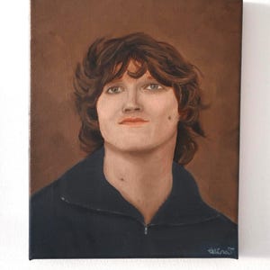 May include: Oil painting portrait of a person with brown hair and a dark blue jacket. The painting is on a canvas with a brown background. The person has fair skin and is looking forward. The artist's signature is in the bottom right corner.
