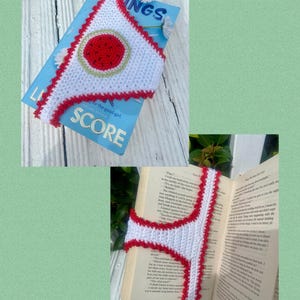 May include: A white crocheted bookmark with a red scalloped edge and a central red circle featuring black seed-like details. The bookmark is shown resting on a blue book cover titled Score and inside an open book with printed text pages.