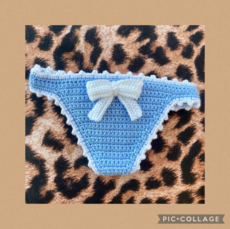 May include: A light blue crochet bikini bottom featuring a white crocheted bow centered on the front. The edges of the garment are finished with a white scalloped crochet trim, providing a decorative border along the waistband and leg openings.