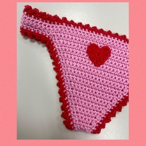 May include: A light pink crochet bikini bottom featuring a vibrant red heart appliqu&eacute; centered on the front. The edges of the garment are finished with a decorative red scalloped crochet trim. The text PIC COLLAGE is visible in the bottom corner.