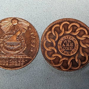May include: Two copper-colored coins with different designs. The first coin features a sun with rays, a compass, and the text "FUGIO 1787 MIND YOUR BUSINESS". The second coin features a circle of linked rings with the text "UNITED WE ARE ONE STATES".