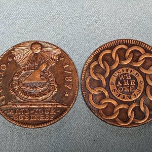 May include: Two copper coins with different designs. The first coin features a sun with rays, a compass, and the text "FUGIO 1787 MIND YOUR BUSINESS". The second coin features a circle of linked chains with the text "UNITED STATES WE ARE ONE".