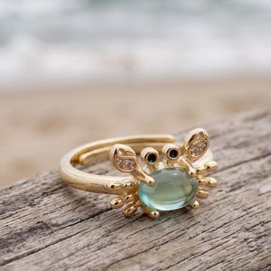 Anel feminino com design de caranguejo fofo, ajustável, em tom dourado, com detalhe verde, perfeito para amantes do oceano.