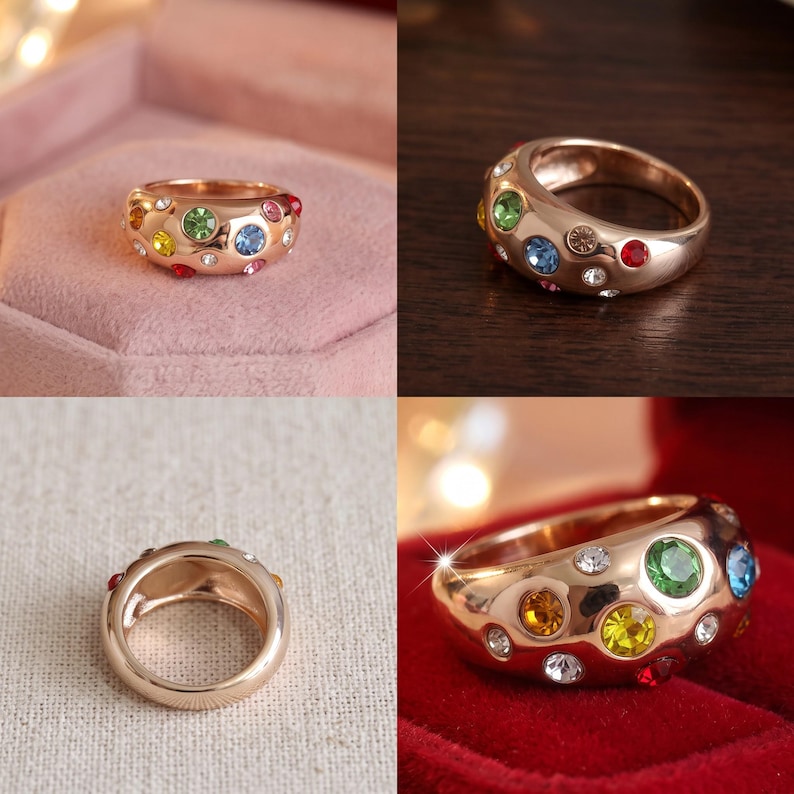 May include: A rose gold-toned ring featuring a wide, polished band embedded with multiple small, round, multi-colored gemstones including green, yellow, blue, red, and clear stones scattered across the surface of the metal band.
