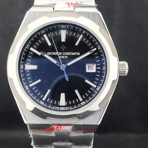 May include: A stainless steel wristwatch with a dark blue face. The watch features a silver bezel with minute markers, silver hands, and the brand name "VACHERON CONSTANTIN GENEVE". The watch band is also stainless steel.