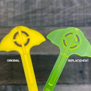 May include: Two plastic tools, one yellow and one green, with a unique shape and a circular design in the center. The yellow tool is labeled "ORIGINAL" and the green tool is labeled "REPLACEMENT".