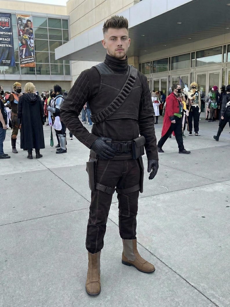 May include: A person in a brown cosplay costume, including a turtleneck, gloves, and boots. The costume features a utility belt, shoulder strap, and pouches. Other cosplayers are in the background.