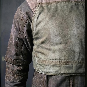 May include: A worn-looking, olive green and brown jacket with quilted detailing. The jacket has a high collar and a layered design, with a padded chest piece. The sleeves are long and feature a quilted pattern. The overall aesthetic suggests a vintage or military-inspired style.