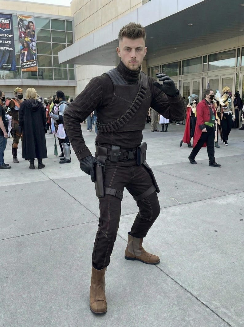 May include: A person in a brown costume with a high collar, shoulder strap, and utility belt. The costume includes gloves, pants, and boots. The person is posing in front of a building with a banner.