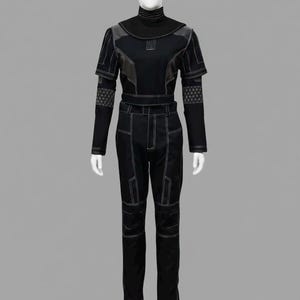 May include: A black long-sleeved jumpsuit featuring a high mock neck collar, structured shoulder panels, and fitted trousers. The garment is accented with prominent white topstitching and a geometric lattice pattern on the lower sleeves.