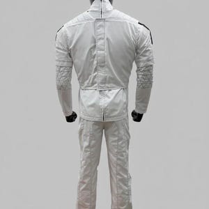 Op de afbeelding: Witte jumpsuit met zwarte accenten, getoond op een mannequin. De outfit heeft gewatteerde details op de mouwen en schouders, een hoge kraag en een getailleerde taille. De broek heeft rechte pijpen en het materiaal lijkt glad, mogelijk synthetisch.