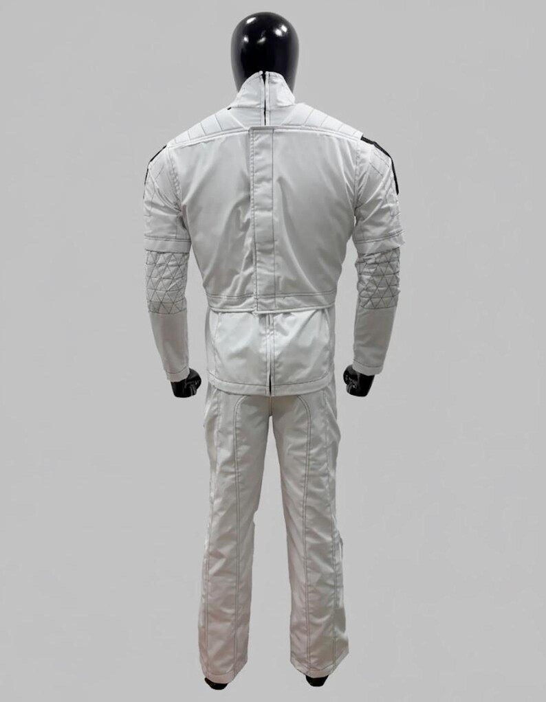 Op de afbeelding: Witte jumpsuit met zwarte accenten, getoond op een mannequin. De outfit heeft gewatteerde details op de mouwen en schouders, een hoge kraag en een getailleerde taille. De broek heeft rechte pijpen en het materiaal lijkt glad, mogelijk synthetisch.