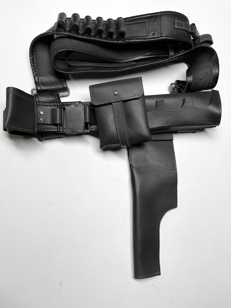 May include: A black leather utility belt with multiple pouches, a holster, and cartridge holders. The belt features a buckle closure and is designed for carrying various items. The leather appears to be smooth and durable.