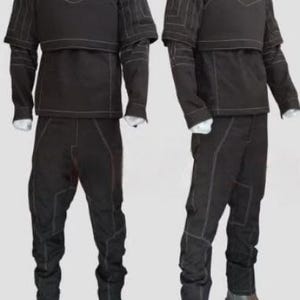 May include: Two black tactical outfits displayed on mannequins. Each outfit includes a high-collared top with a chest protector, long sleeves, and matching pants. White stitching accents the seams. The outfits are paired with brown boots.