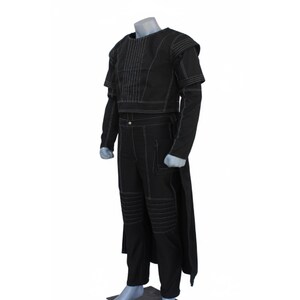 Op de afbeelding: Een zwarte set bestaande uit een top met lange mouwen en een bijpassende broek met opvallende witte stiksels. De top heeft gestructureerde schouders en verticale stiksels op de borst. De broek bevat knievullingdetails en een lang achterpaneel.