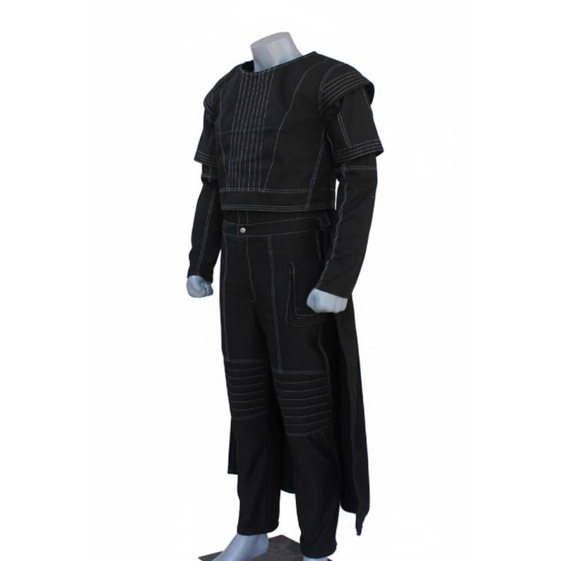 Op de afbeelding: Een zwarte set bestaande uit een top met lange mouwen en een bijpassende broek met opvallende witte stiksels. De top heeft gestructureerde schouders en verticale stiksels op de borst. De broek bevat knievullingdetails en een lang achterpaneel.