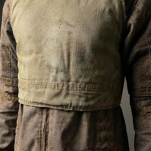 May include: A worn, brown jacket with a quilted design on the sleeves and a contrasting, lighter-colored chest panel. The jacket appears to be made of a durable, possibly canvas-like material, suggesting a workwear or utilitarian aesthetic.