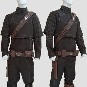May include: Two complete black costumes with brown accents are displayed on mannequins. Each outfit includes a high-collared top, pants, a belt with pouches, and a shoulder strap. The costumes have white stitching details and brown holsters.