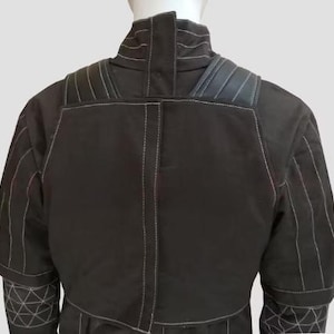 May include: A black jacket with white stitching details. The jacket features a high collar, padded shoulders, and geometric patterns on the sleeves. The back view showcases the tailored design and construction of the garment.