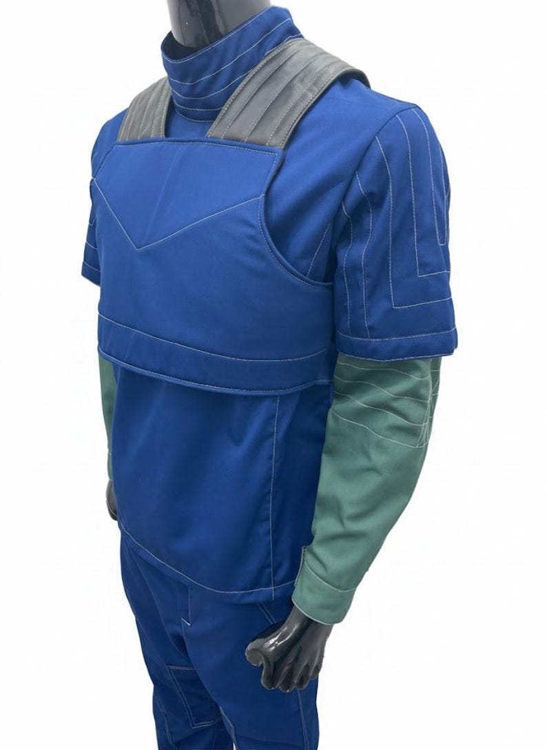May include: Blue and green short-sleeve jumpsuit with gray shoulder padding. The jumpsuit has white stitching details and a high collar. The sleeves are green, and the body is blue. The jumpsuit is displayed on a black mannequin.