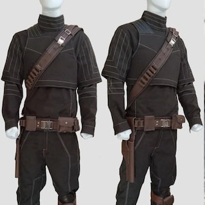 May include: Two black costumes with brown accents are displayed on mannequins. Each outfit includes a high-collared top, pants, a belt with pouches, and a shoulder strap. The tops have white stitching details, and the pants have knee pads.