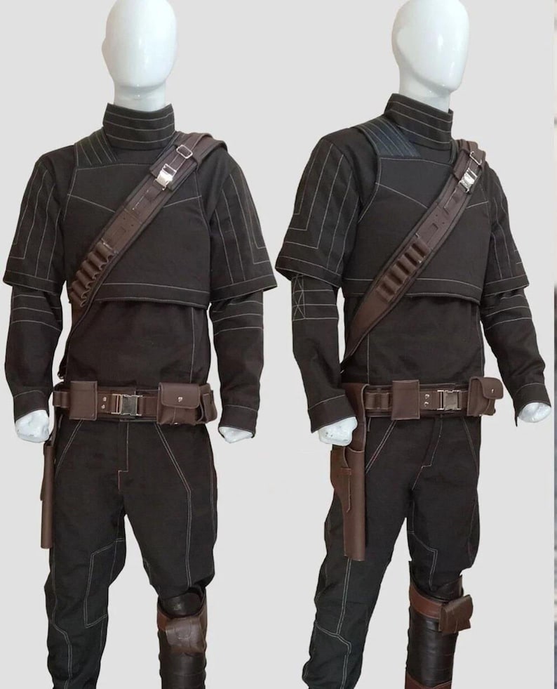May include: Two black costumes with brown accents are displayed on mannequins. Each outfit includes a high-collared top, pants, a belt with pouches, and a shoulder strap. The tops have white stitching details, and the pants have knee pads.